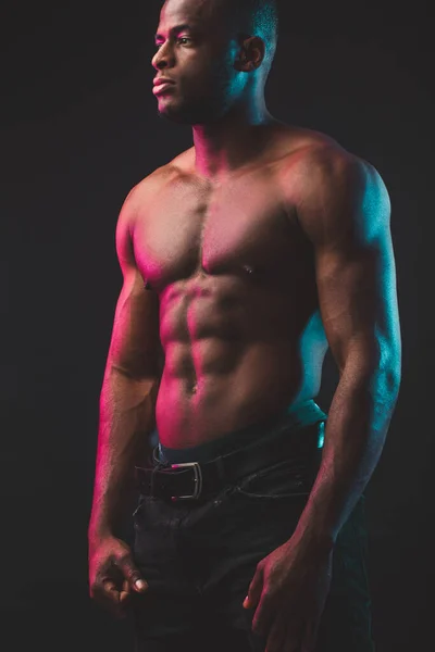 Fit African man with amazing abs and naked torso, isolated on dark background.
