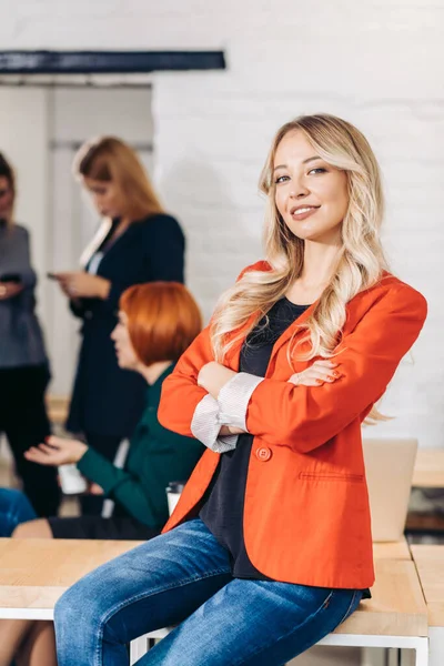Blond zakenvrouw glimlacht op camera met collega 's werken op de achtergrond — Stockfoto