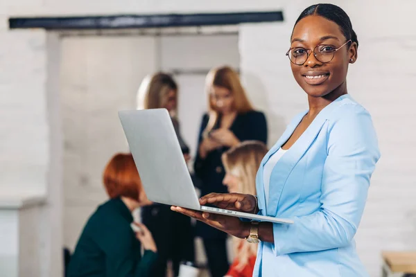 business black woman adjusting laptop, standing with office colleagues behind