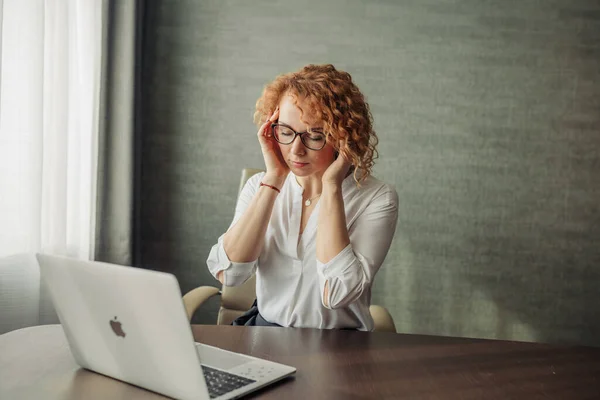 Overworked jovem mulher mantendo os olhos fechados sentado com laptop no local de trabalho — Fotografia de Stock