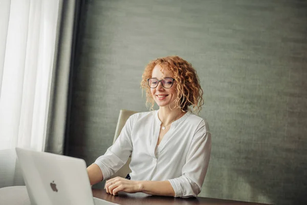 Boldog vörös hajú nő szemüveg dolgozik laptop ül a szürke fal — Stock Fotó