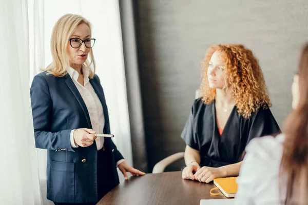 Marknadsföringsexperter sitter runt bordet och tittar på kvinnliga talare på mötet. — Stockfoto