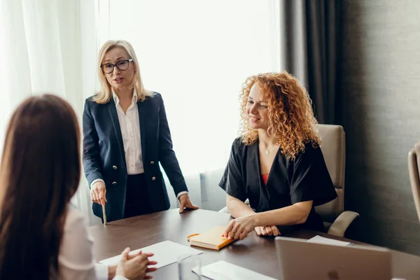 Expertos en marketing se sientan alrededor de la mesa y miran a la mujer en la reunión. — Foto de Stock