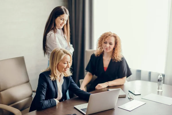 Tres diseñadores femeninos se reúnen en el interior de la oficina moderna usando computadora portátil. — Foto de Stock