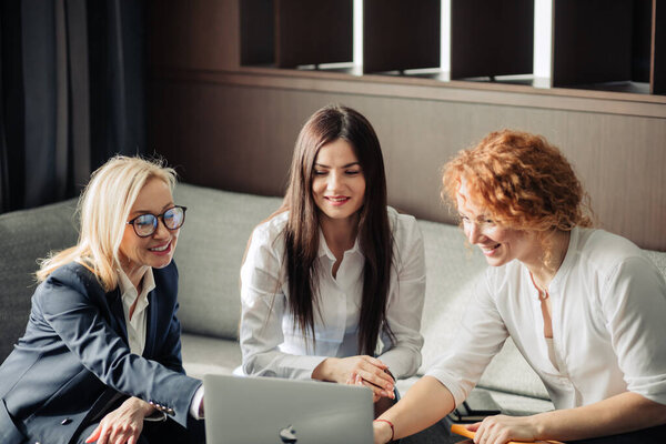 Three focused business women with different hairstyle work together in office.