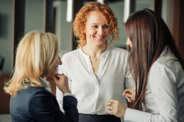 Tre positiva affärskvinnor i vita formella skjortor chattar i kontorslobbyn. — Stockfoto