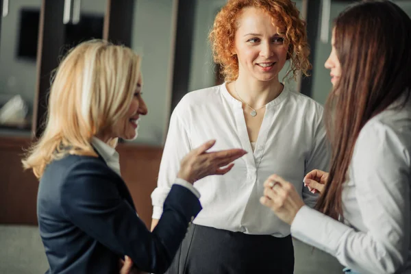 Tre positiva affärskvinnor i vita formella skjortor chattar i kontorslobbyn. — Stockfoto