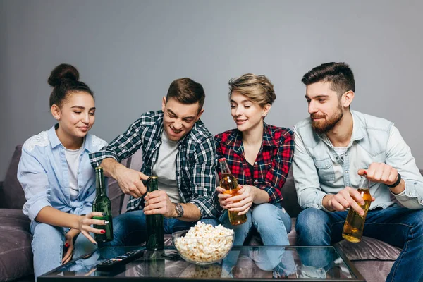 Amigos alegres van a beber cerveza mientras están sentados en el sofá en casa — Foto de Stock