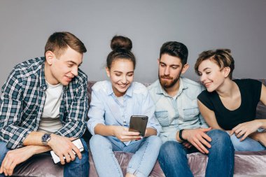 Neşeli genç erkekler ve kadınlar akıllı telefondan film izliyorlar.
