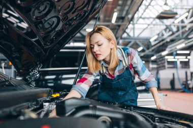 Genç, hoş bayan tamirci motor kaputunun altına bakıyor.