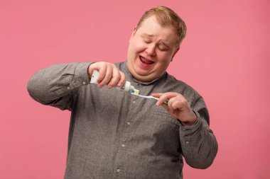 Mutlu adam pembe arka planda dişlerini canlı duygularla fırçalıyor.