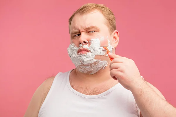 Homem gordo parece irritado, sentindo dor ou irritação, ao fazer a barba com navalha. — Fotografia de Stock