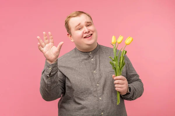Hombre divertido con flores va a hacer propuesta, tiene mirada alegre y sonrisa ingenua —  Fotos de Stock