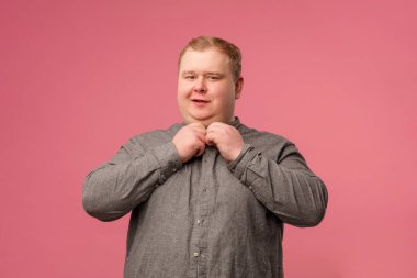 Neşeli adam kameraya bakarken gri gömleğini pembeye iliştiriyor.