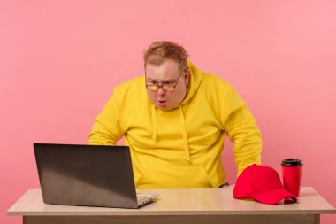 Şişman vücutlu şok olmuş bir adam ağzını açar ve dizüstü bilgisayarına bakar..