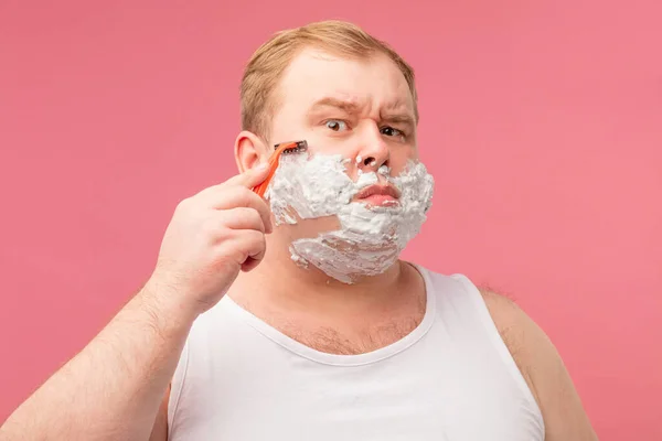 Primer plano del hombre adulto disgustado afeitándose con espuma y afeitadora aislada en rosa —  Fotos de Stock
