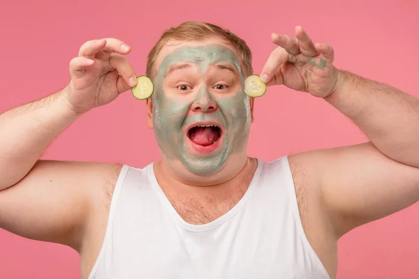 Alegre hombre divertido tiene máscara de arcilla, expresa emociones positivas, aislado en rosa. — Foto de Stock