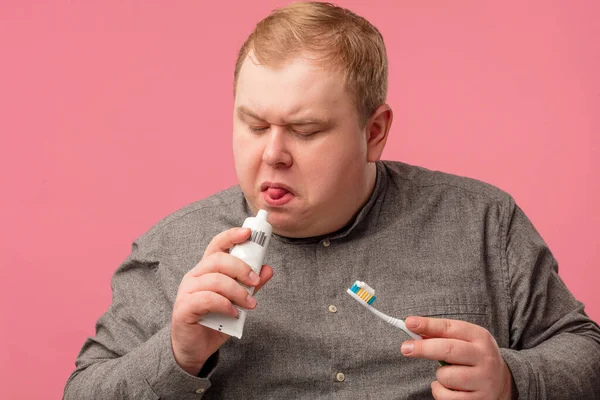 Gordito hombre de mediana edad en camisa gris prueba una nueva pasta de dientes que huele extraño. — Foto de Stock