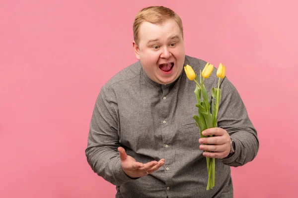 Lindo hombre emocional mira a tres tulipanes en las manos con la boca abierta y asombro —  Fotos de Stock