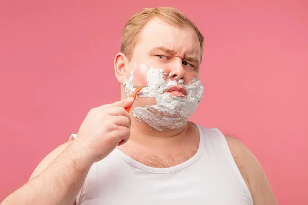 Close-up de homem adulto descontente barbear com espuma e navalha isolado em rosa — Fotografia de Stock