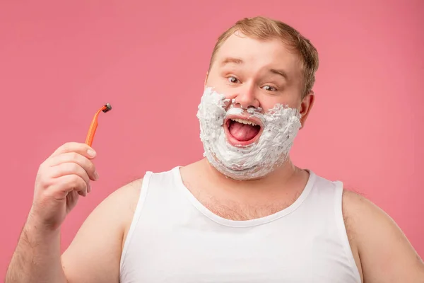 Feliz homem gordo com espuma de barbear em seu rosto e navalha isolada em rosa — Fotografia de Stock