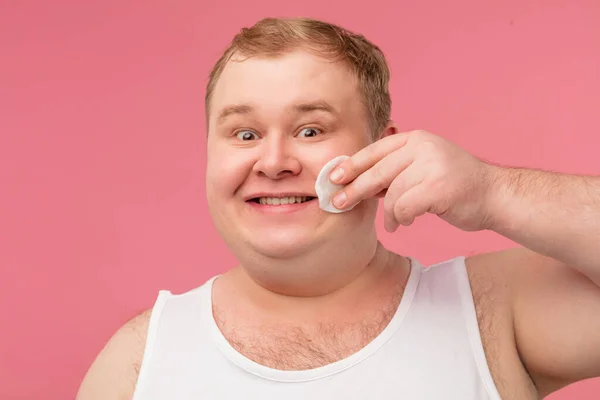 Divertido hombre alegre jouful en camiseta aplicando tónico por almohadilla de algodón en la cara — Foto de Stock
