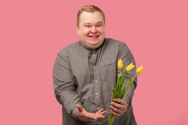 Hombre divertido con flores va a hacer propuesta, tiene mirada alegre y sonrisa ingenua —  Fotos de Stock