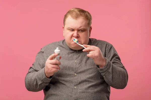 Emocional hombre disgustado y desconcertado cepillarse los dientes con una nueva pasta dental. — Foto de Stock