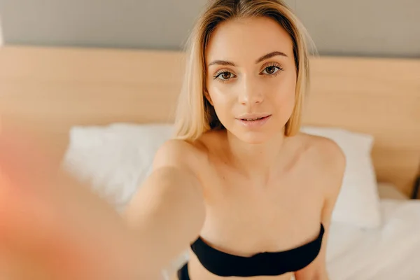 Sensual blonde woman in black underwear looking at camera while lying in bed — Stock Photo, Image