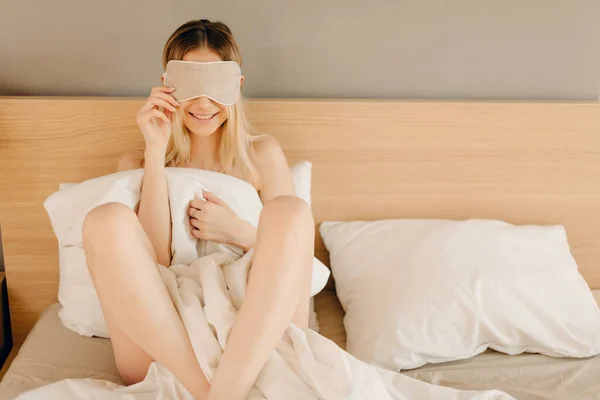 Femme blonde cachant son corps sous la couverture et ses yeux sous le masque de sommeil — Photo