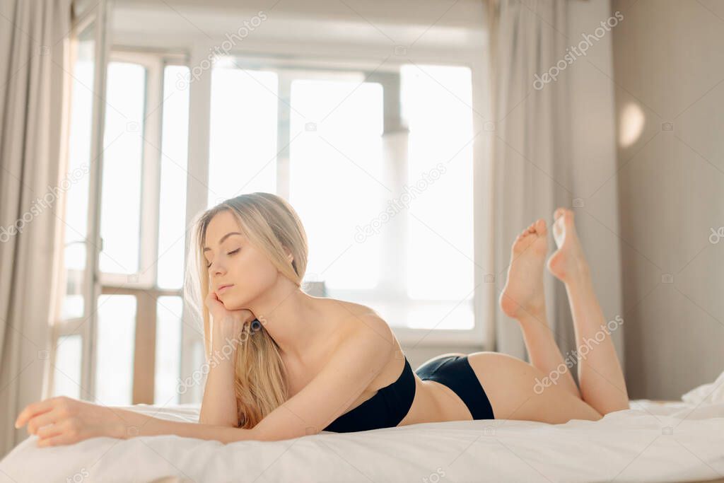 Happy morning. Smiling pretty young blonde woman relaxing in white bed