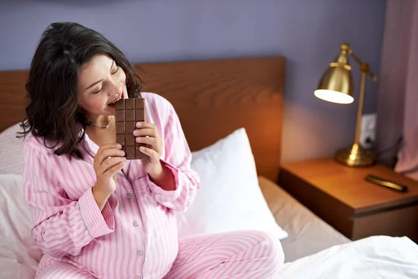Sweet craving during pregnancy concept, pregnant woman with chocolate on bed — Stock Photo, Image
