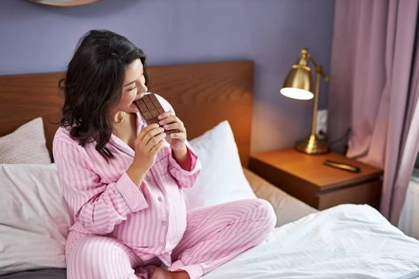 Mujer embarazada toma un bocado de chocolate con leche — Foto de Stock