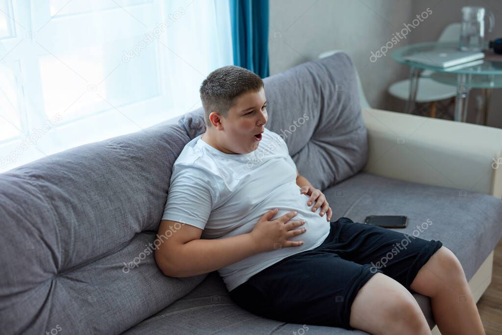 fat teenager boy has stomach ache after junk food