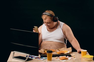 Koca göbekli şişman adam bilgisayarı kullanırken bir telefon görüşmesi yapıyor.