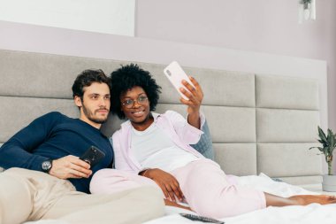 Genç ve güzel bir çift yatakta uzanıyor ve selfie çekiyorlar.