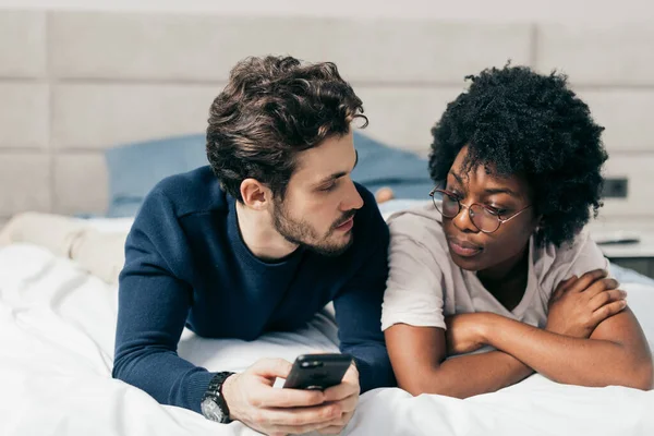 Gemengd ras familie paar chatten met vrienden liggen in bed, gekleed casual — Stockfoto