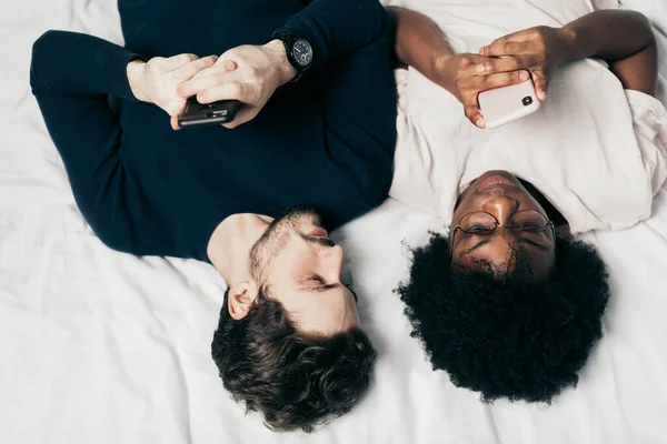 Mixed race family couple chat with friends lying in bed, dressed casual — Stock Photo, Image