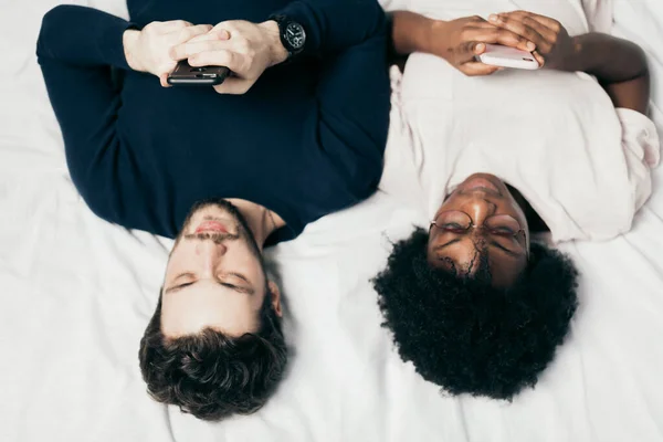 혼합 인종 부부는 평상복을 입고 침대에 누워 있는 친구들 과대화 한다 — 스톡 사진