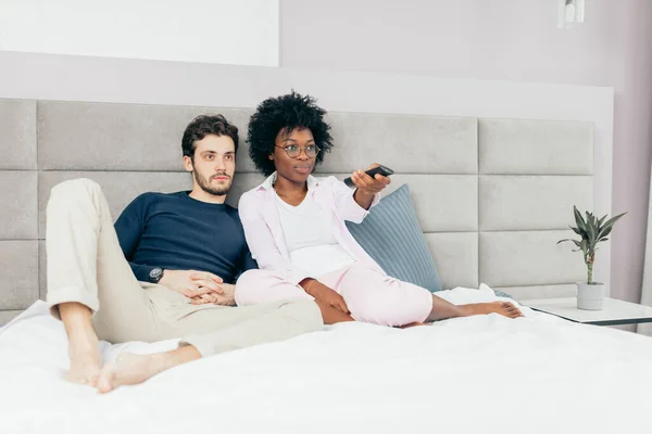 Vegyes verseny pár pihen az ágyon, és TV-t néznek együtt a nap-off — Stock Fotó