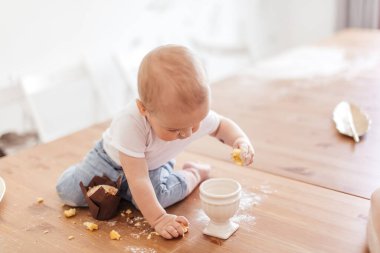 Küçük fırıncı çocuk un yayılmış halde masada oturarak kek yapmaya yardım ediyor..