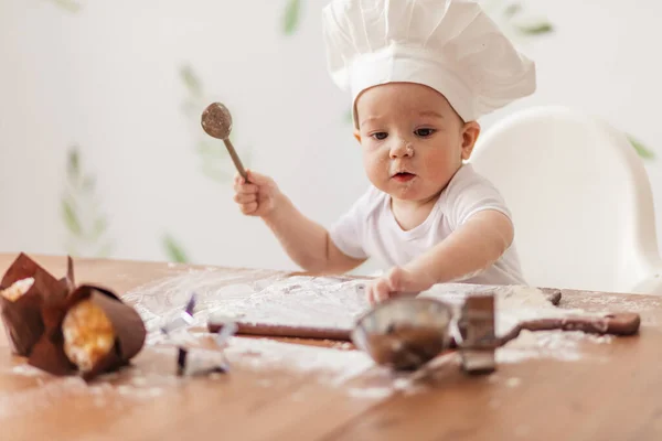Infant cook baby portrait wearing chef hat playing with dough at kitchen table. — Stock Photo, Image