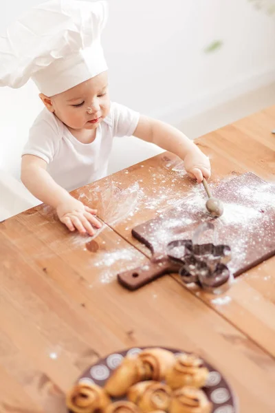 Happy cute little baby boy in a cook cap playing with flour at home kitchen — Stock Photo, Image