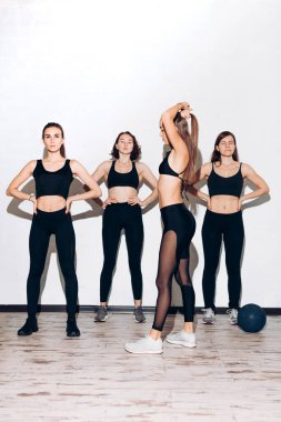 Genç bir kız saçını topuz gibi tararken bir grup insan spor yapıyor.