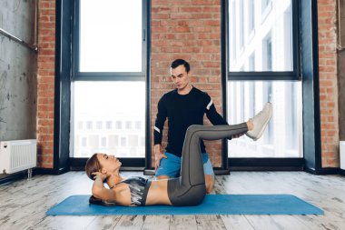 Karın egzersizi yapan kaslı bir kadın. Kişisel antrenör onu kontrol ederken.