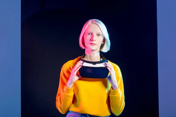 Приваблива блондинка тримає гарнітуру VR і дивиться на камеру — стокове фото