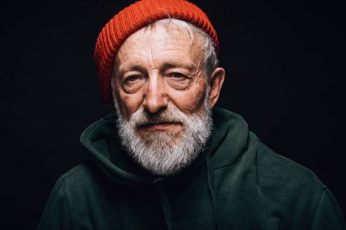 Yaşlı deneyimli gri sakallı adam kameraya kendine güvenen bir ifadeyle bakıyor..