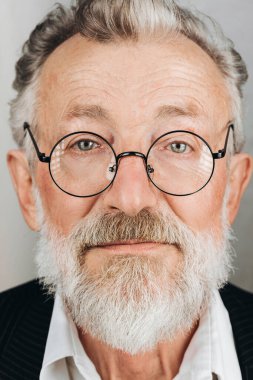 Yuvarlak gözlü beyaz yaşlı adam kameraya tarafsız bir ifadeyle bakıyor..