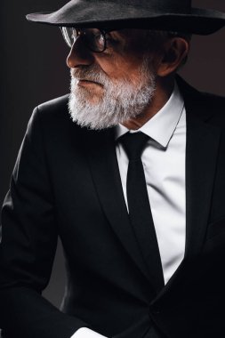 Fötr şapkanın arkasına saklanan, İngiliz casusu rolünü oynayan yaşlı bir erkek oyuncu..