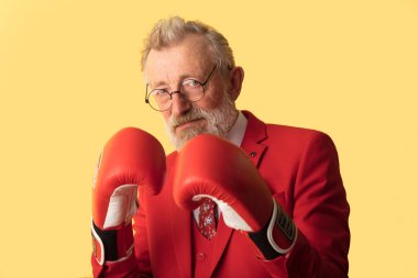 Kırmızı takım elbiseli kıdemli bir işadamı ve savunma pozisyonunda duran kırmızı boks eldivenleri.